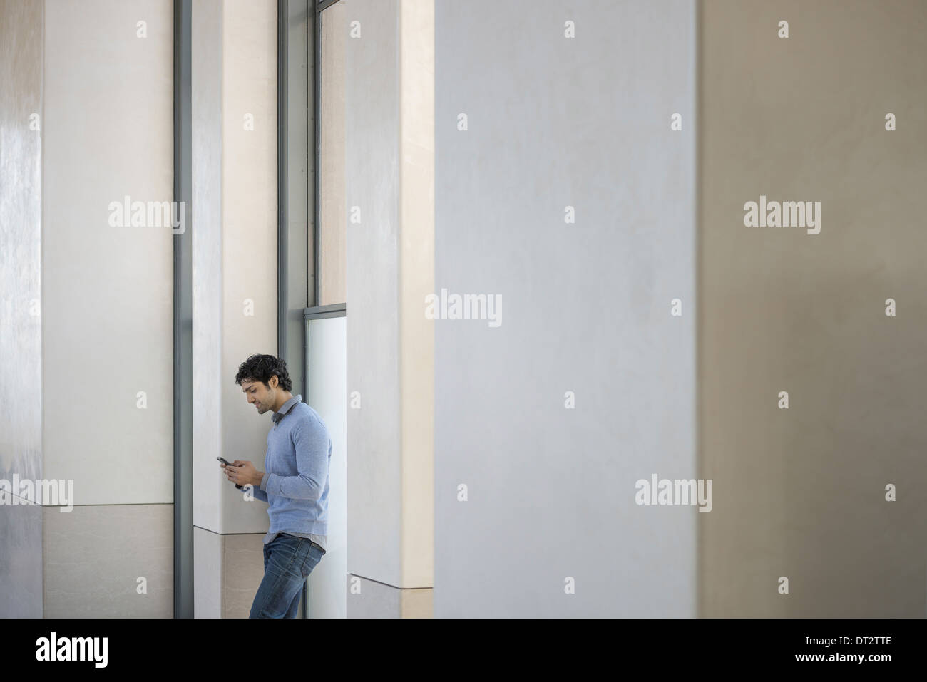 Urban Lifestyle A man in a blue sweater using his mobile phone An empty building Stock Photo