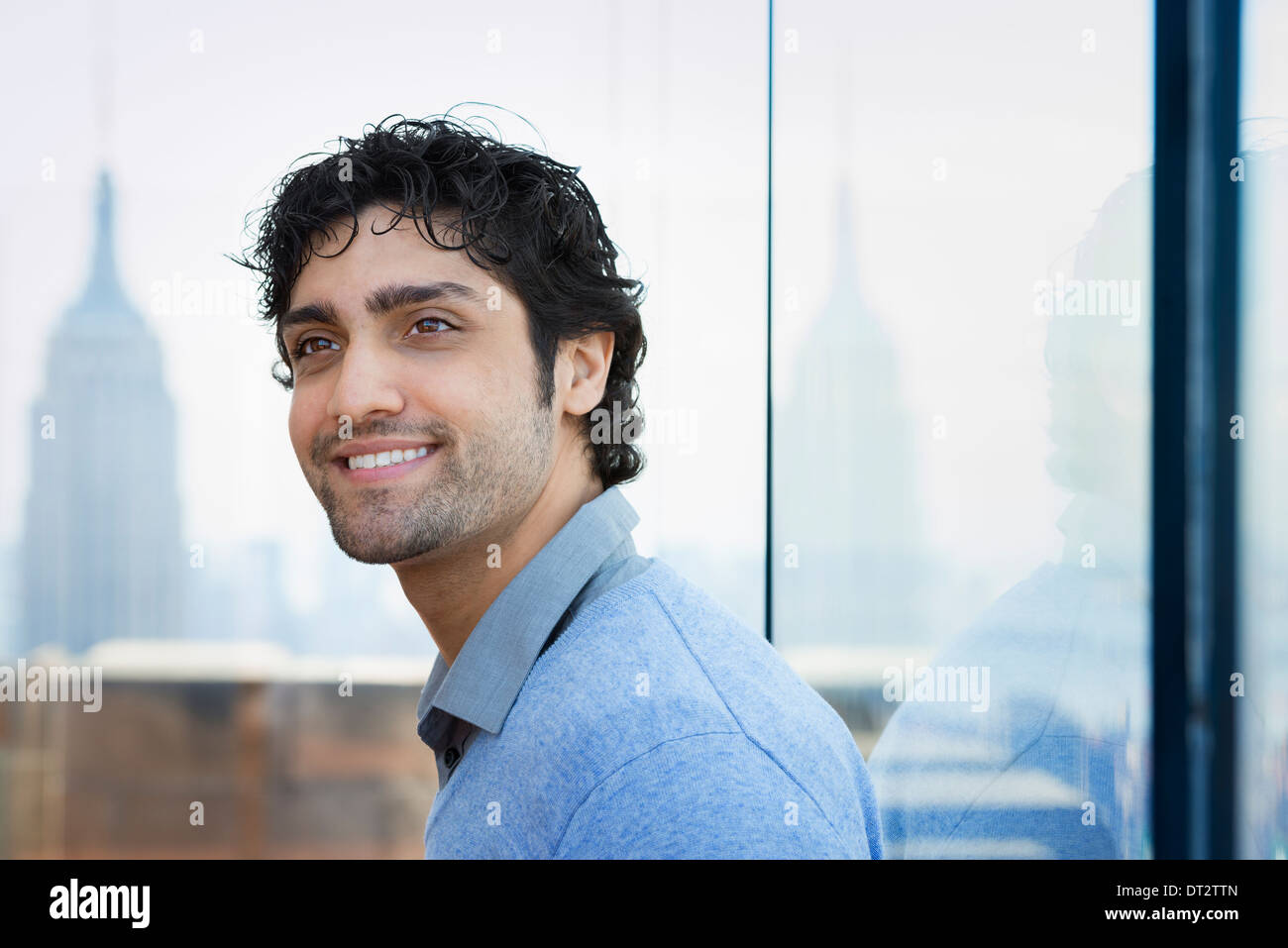 Urban Lifestyle A young man with black curly hair wearing a blue shirt in the lobby of a building Stock Photo
