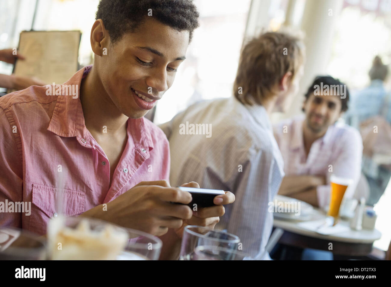 Urban Lifestyle Three young men in a cafe One checking his smart phone Two talking at a table Stock Photo