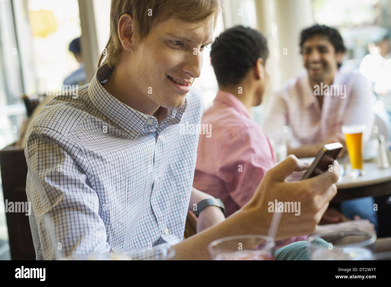 Urban Lifestyle Three young men in a cafe One checking his smart phone Two talking at a table Stock Photo