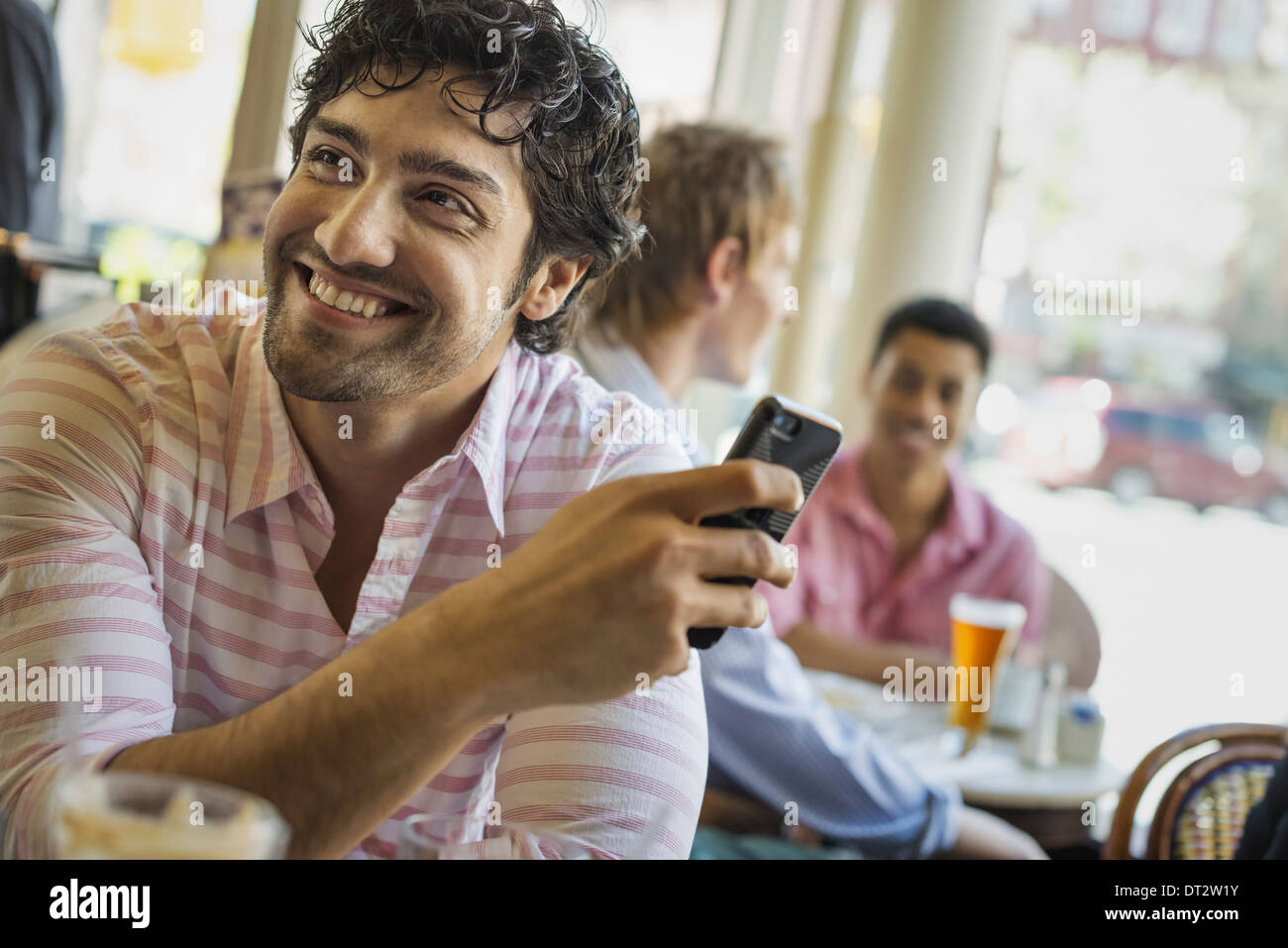Urban Lifestyle Three young men around a table in a cafe One using his smart phone Stock Photo