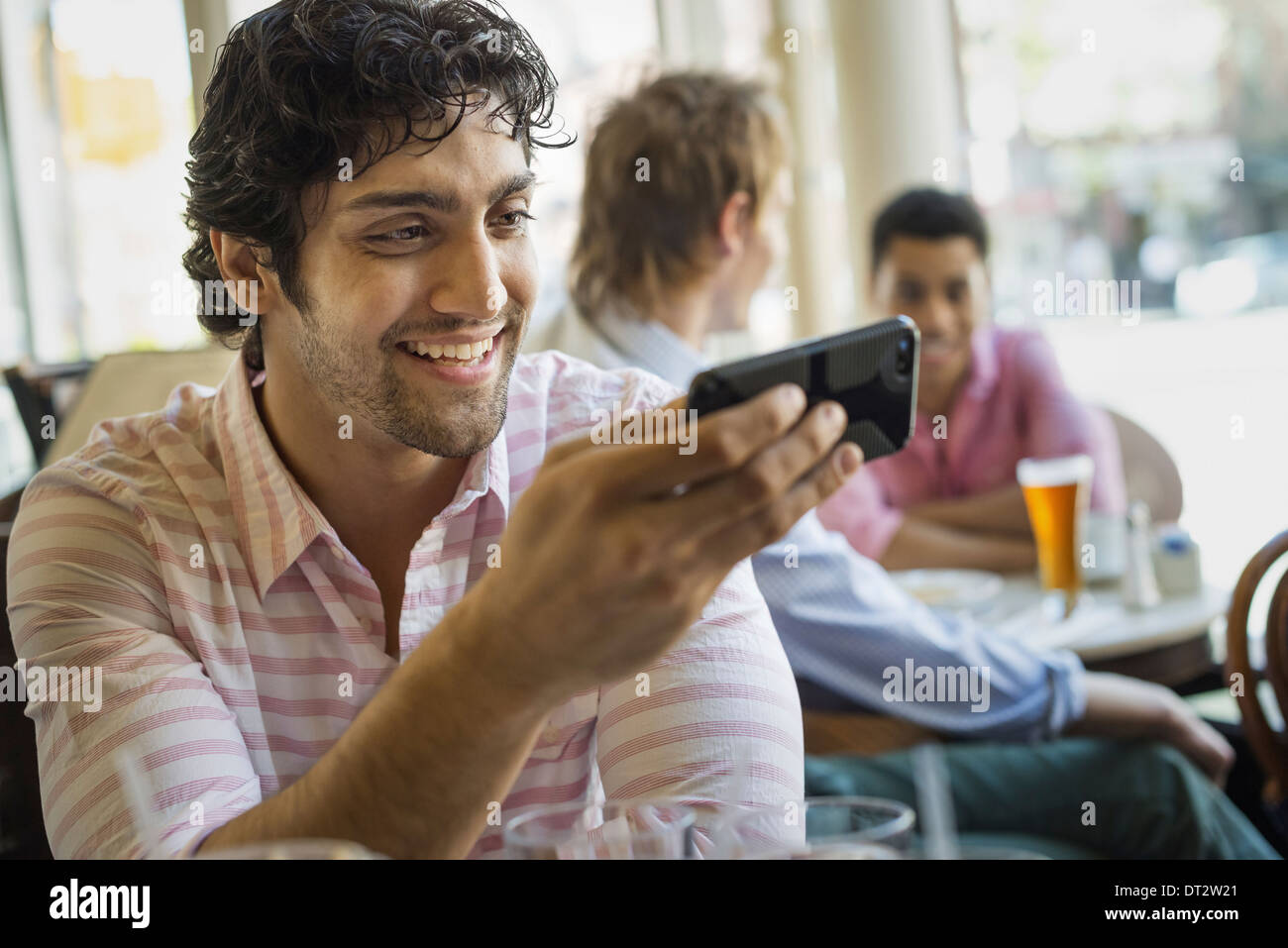 Urban Lifestyle Three young men around a table in a cafe One using his smart phone Stock Photo
