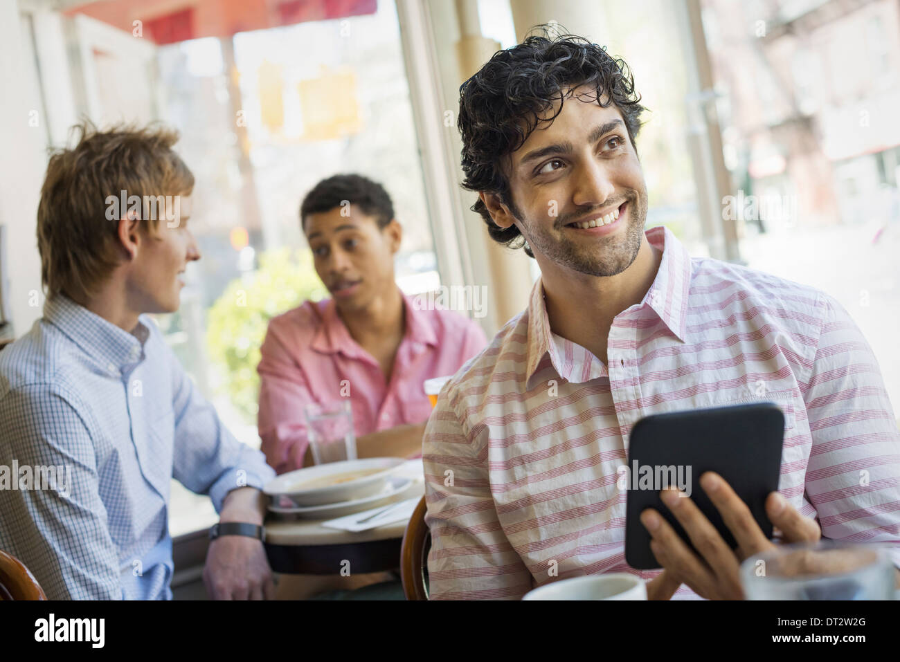 Urban Lifestyle Three young men around a table in a cafe One holding a digital tablet Stock Photo