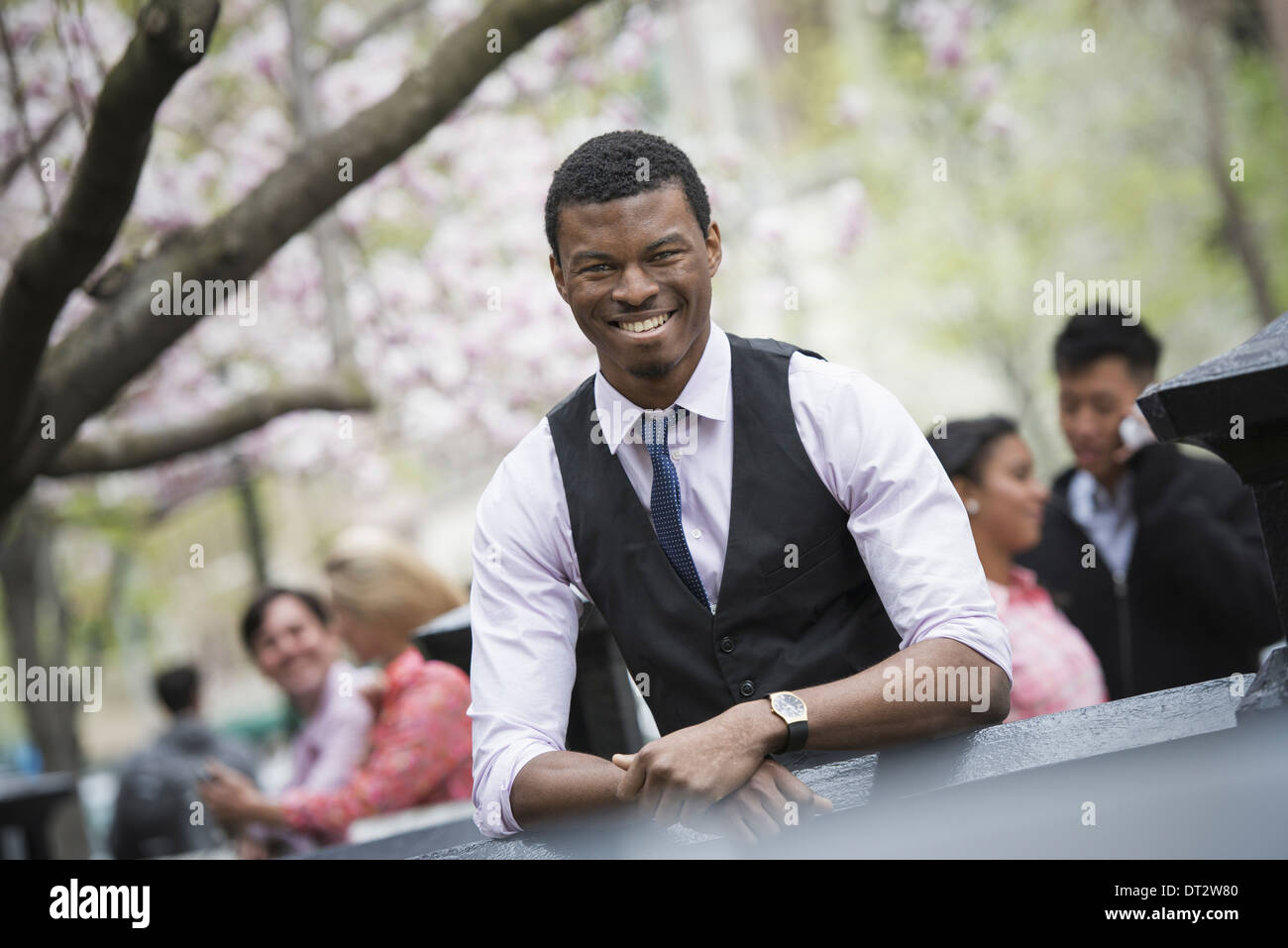 View over cityYoung people outdoors in a city park A man sitting down with four people in the group behind him Stock Photo