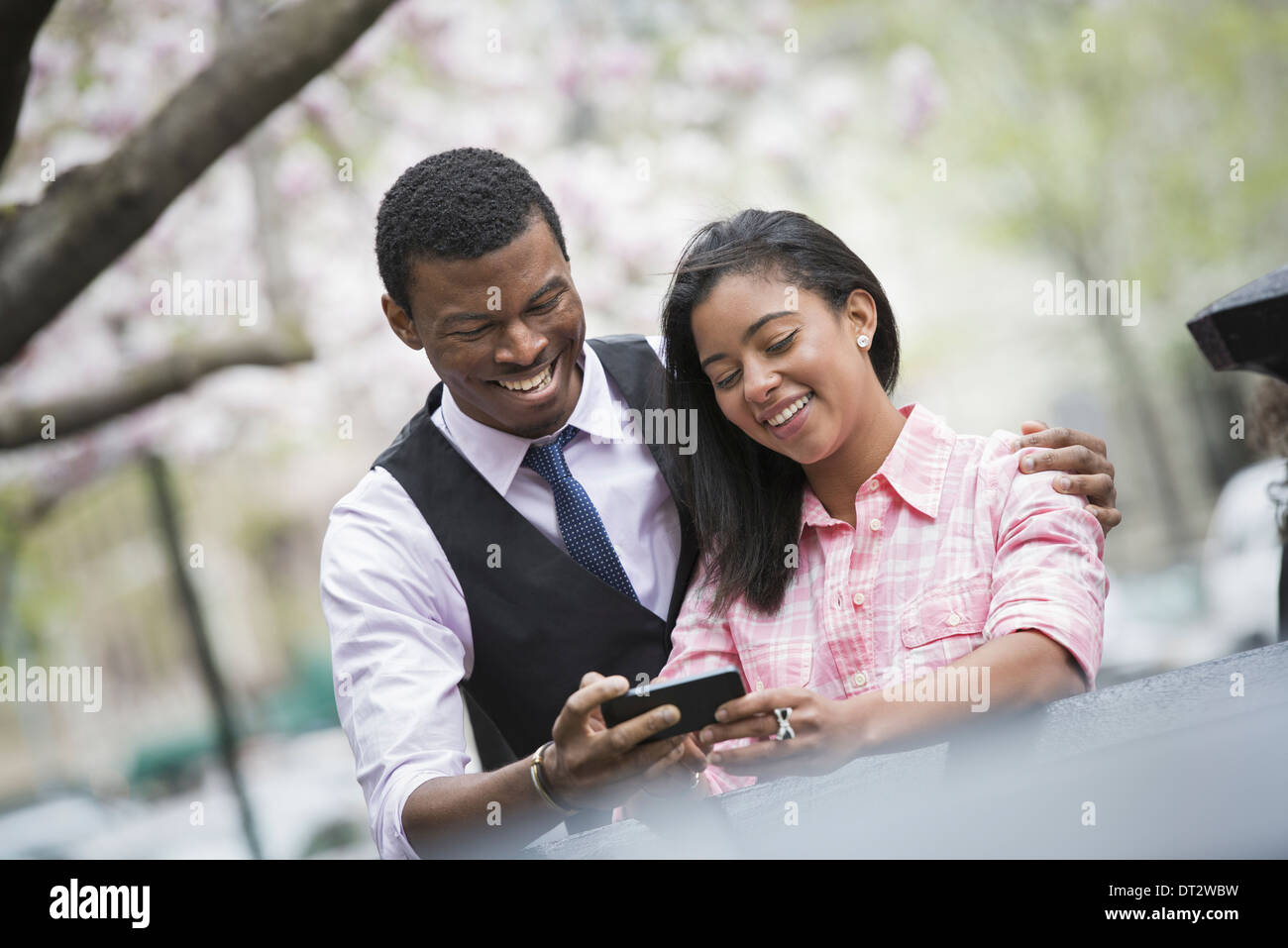 View over cityYoung people A couple side by side with his arm around her shoulders looking at a smart phone and smiling Stock Photo