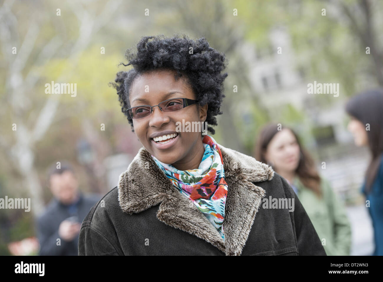 A group of people in a city park A young woman in a coat with a large collar smiling and looking at the camera Stock Photo