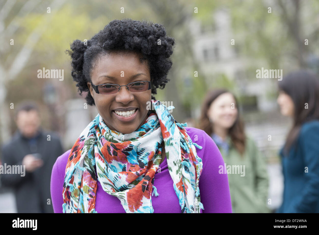 A group of people in a city park A young woman smiling wearing a purple shirt and floral scarf Stock Photo