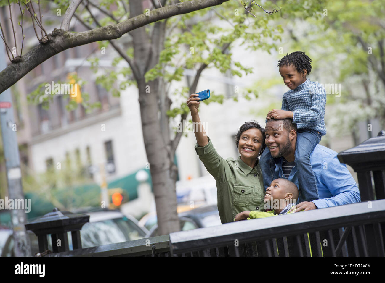 A boy riding on his father's shoulders and a woman using a smart phone taking a selfy picture Stock Photo