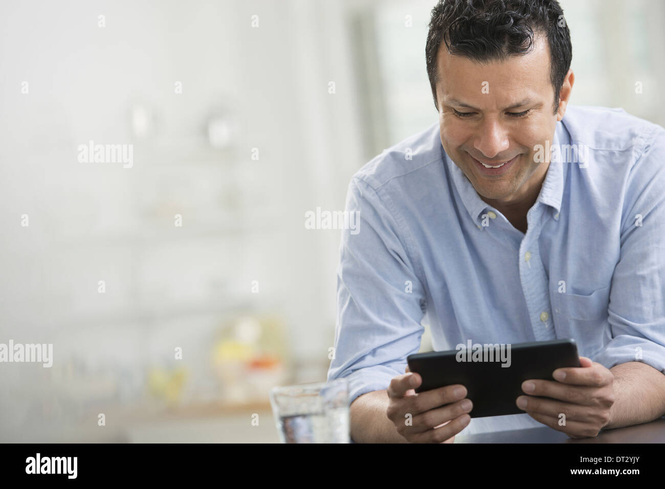 A man in a blue shirt leaning on a desk holding a digital tablet Stock Photo
