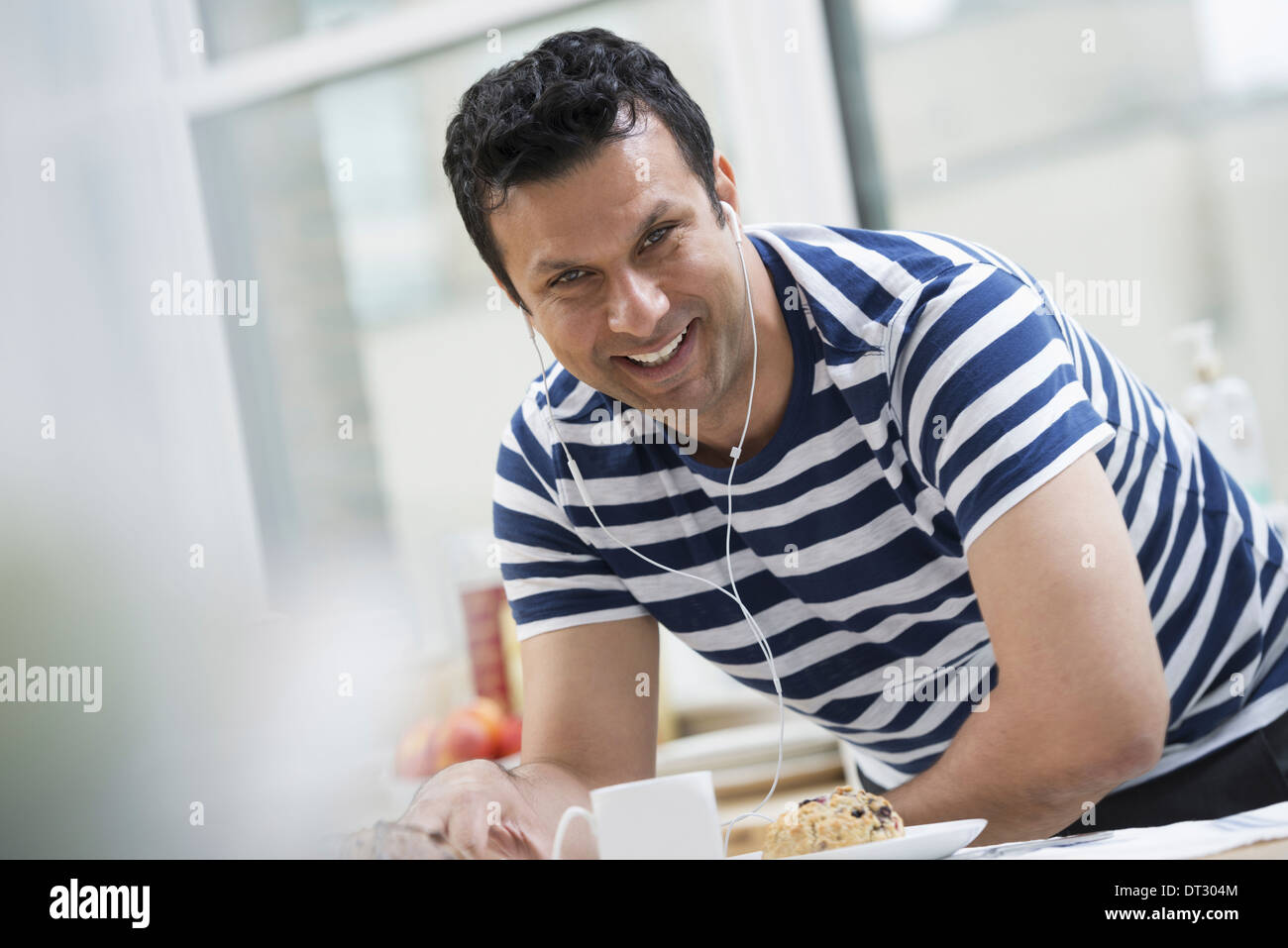 An office or apartment interior in New York City A man in a striped tee shirt leaning on the breakfast bar Stock Photo