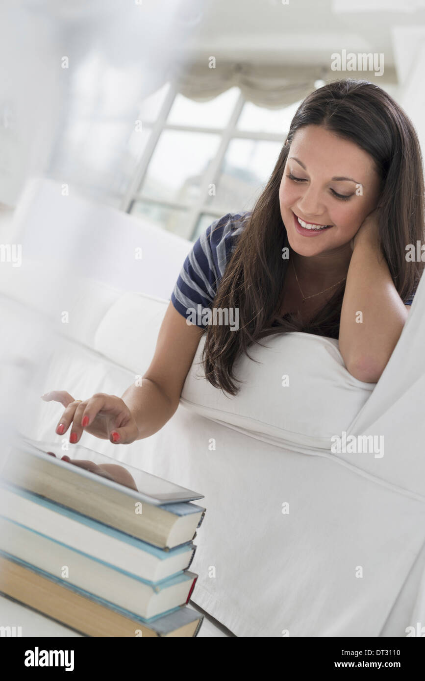 woman lying on her front on a sofa in a quiet airy office environment using a smart phone Stock Photo