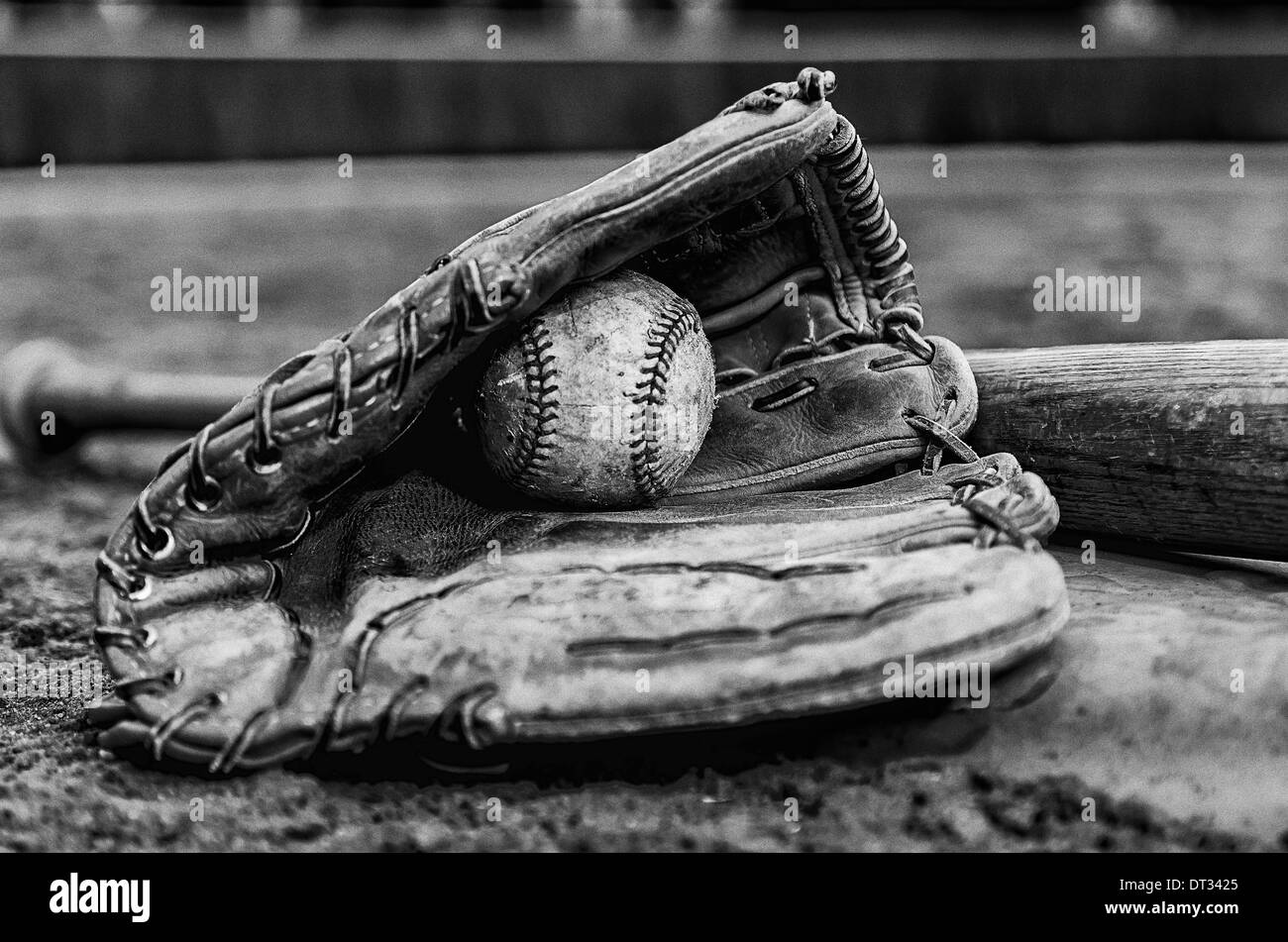 Baseball glory days with ball in glove and bat on base on field. Monochrome image with outfield wall in background. Stock Photo