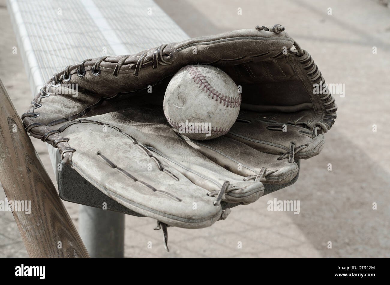 Baseball times gone by with ball and glove on bench in dugout with bat. Stock Photo