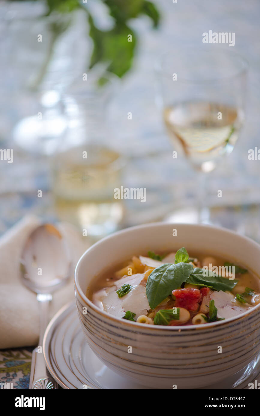 A bowl of pasta and bean soup set on a table with white wine Stock Photo