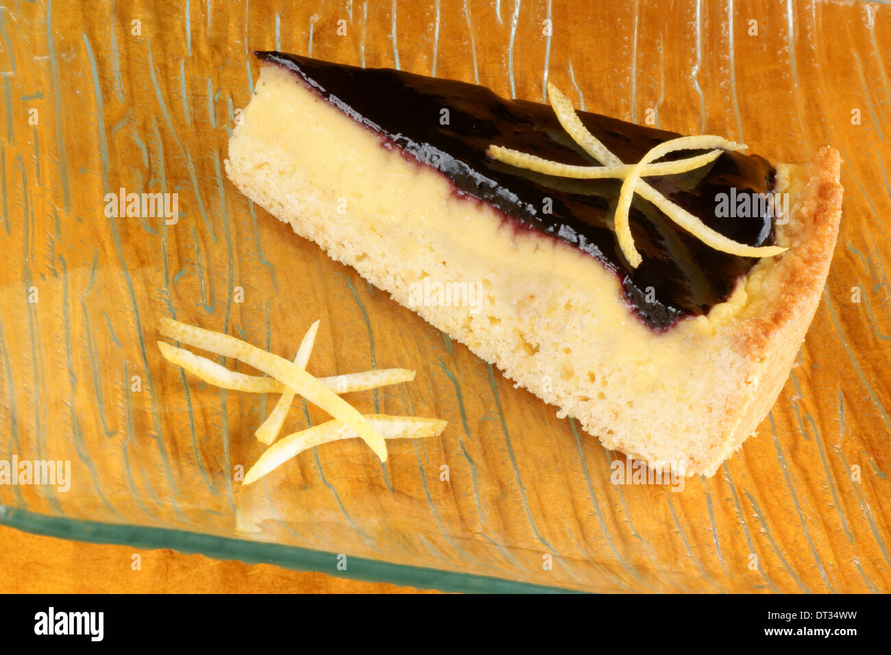 Slice of blueberry jam and custard cream tart served on a glass plate with lemon zest, over an