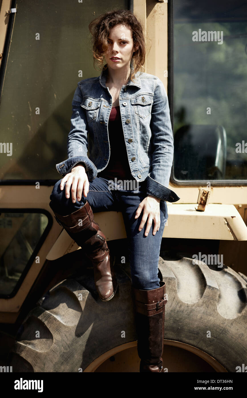 A young woman in denim jacket and boots on the hood of a tractor Stock Photo
