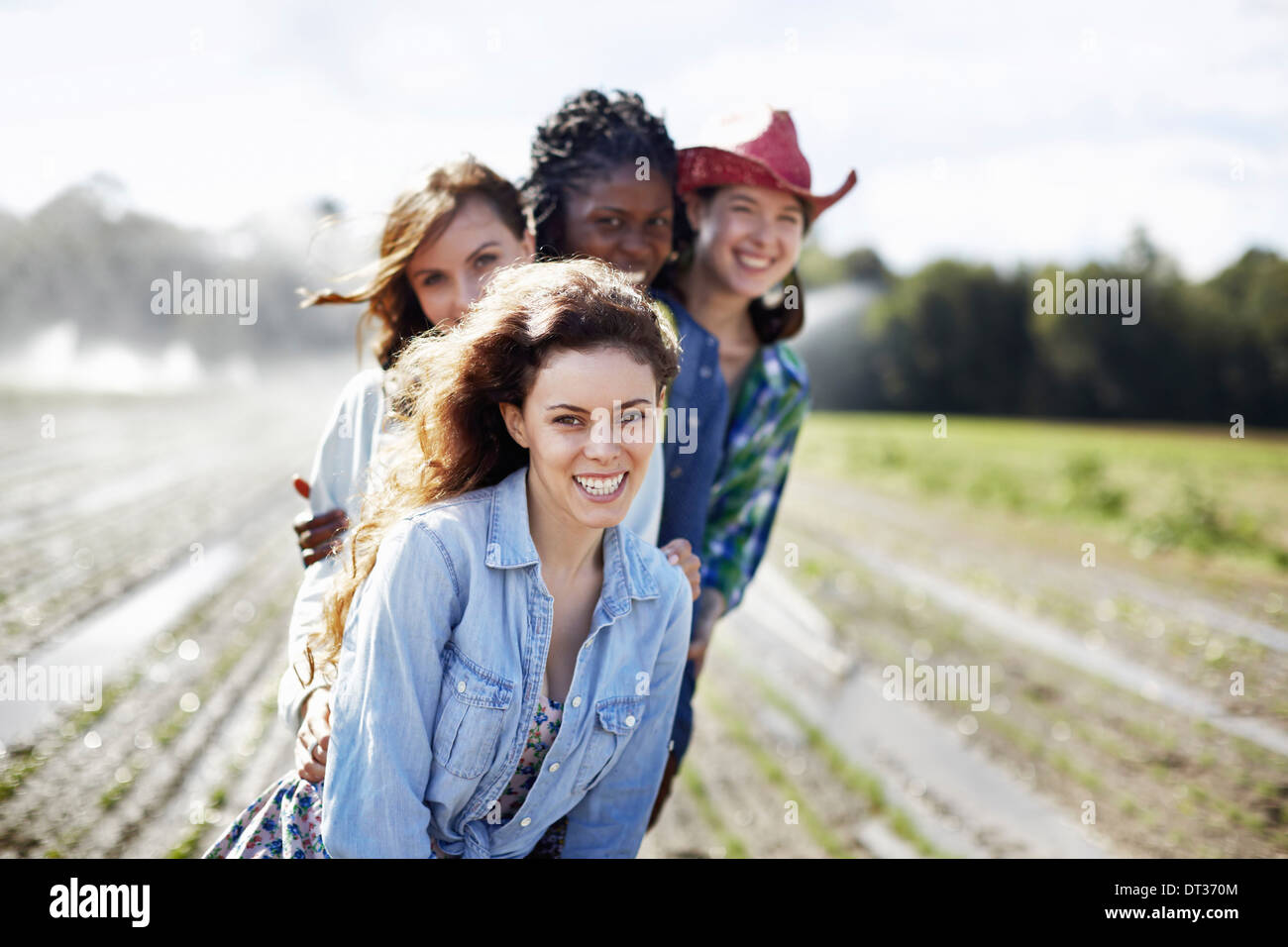 Four young women in a field full of seedlings an organic crop with sprinklers spraying water in the background Stock Photo