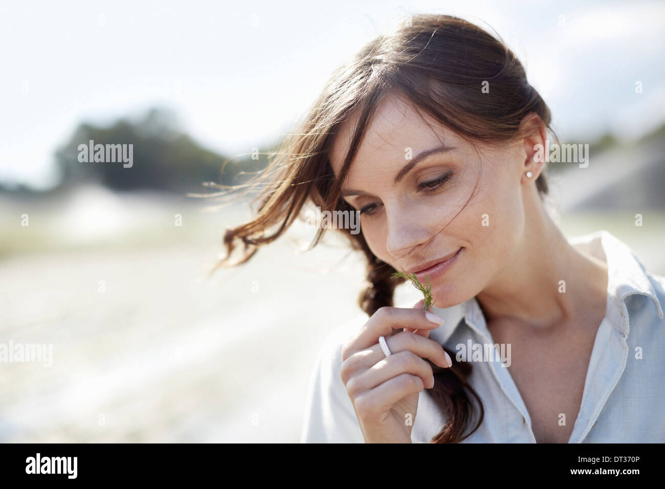 A young woman with windblown hair with a small green sprig of plant material in her hand Stock Photo