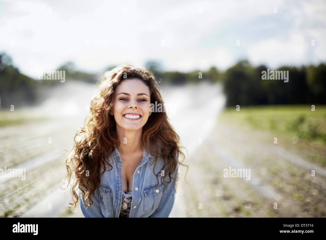 A young woman in denim jacket standing in a field irrigation sprinklers working in the background Stock Photo