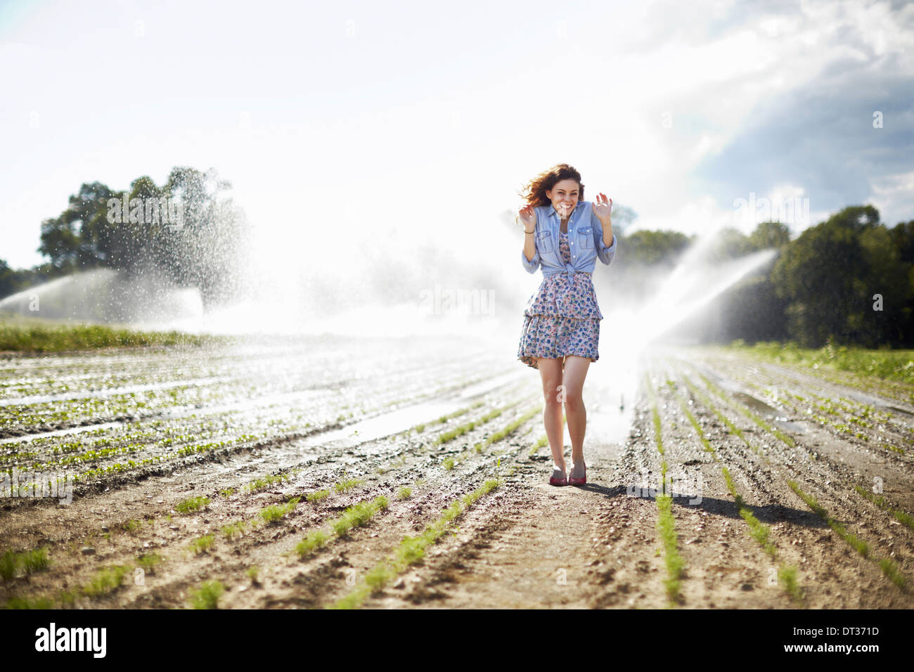 A young woman in denim jacket standing in a field irrigation sprinklers working in the background Stock Photo