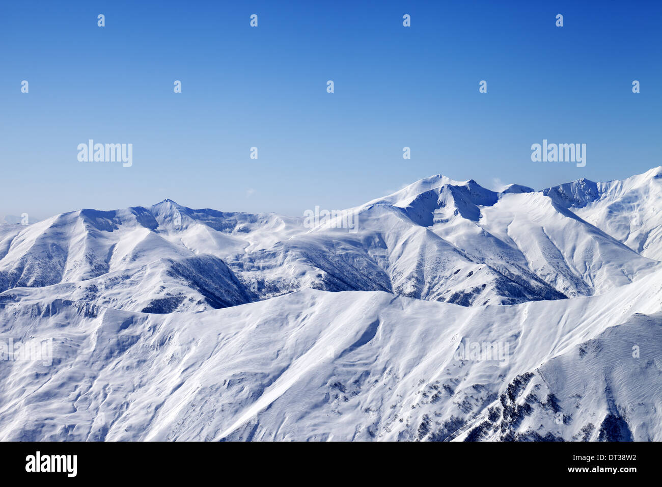 Snowy winter mountains and blue sky, view from ski slope. Caucasus Mountains, Georgia, ski resort Gudauri. Stock Photo