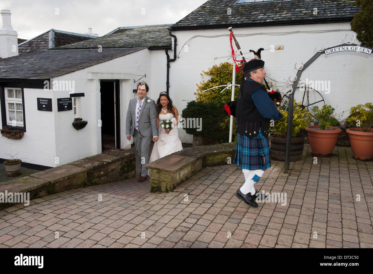 A newly married couple walk from The Old  Blacksmith's Shop in Gretna Green, Scotland, preceded by a piper Stock Photo