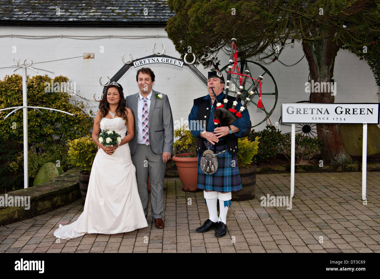 A newly married couple pose outside The Old  Blacksmith's Shop in Gretna Green, Scotland, accompanied by a piper Stock Photo