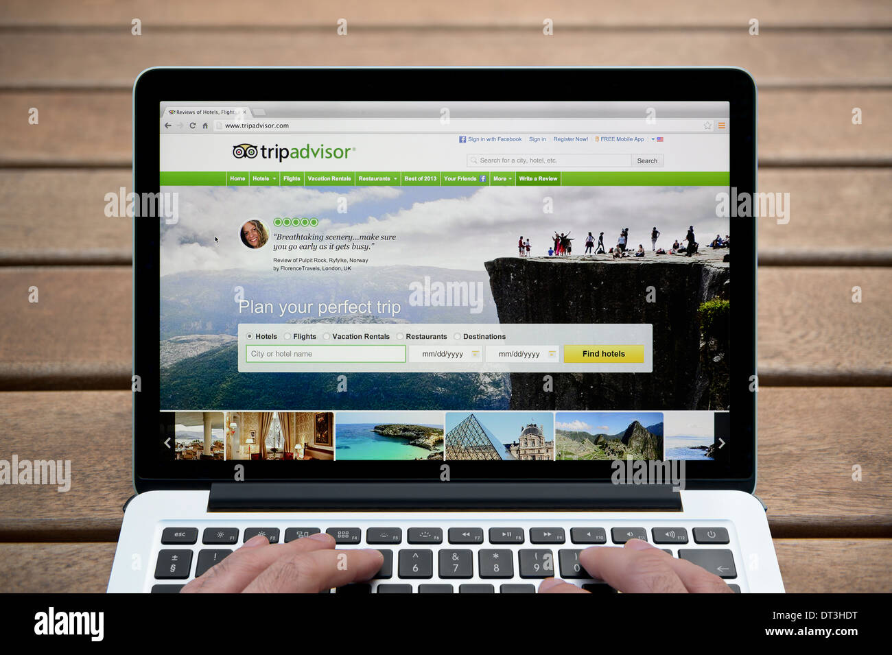 The Trip Advisor website on a MacBook against a wooden bench outdoor background including a man's fingers (Editorial use only). Stock Photo