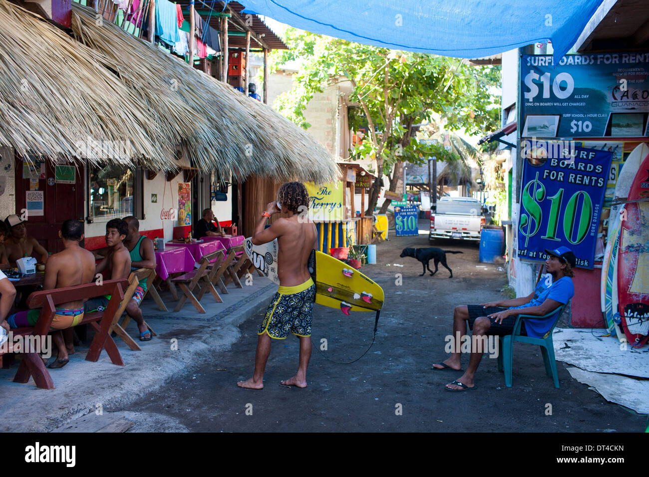 Local surfer banter in the narrow streets before surfing in El Tunco, a beach town in El Salvador popular with surfers. Stock Photo