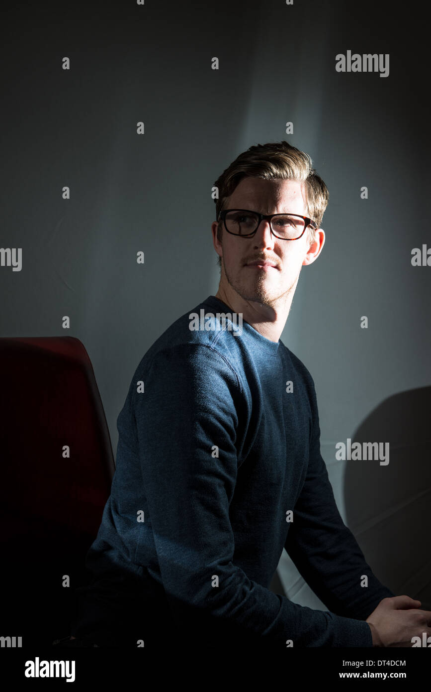 A young man wearing glasses and photographed on black with a shaft of flash light looks past the camera as though thinking. Stock Photo