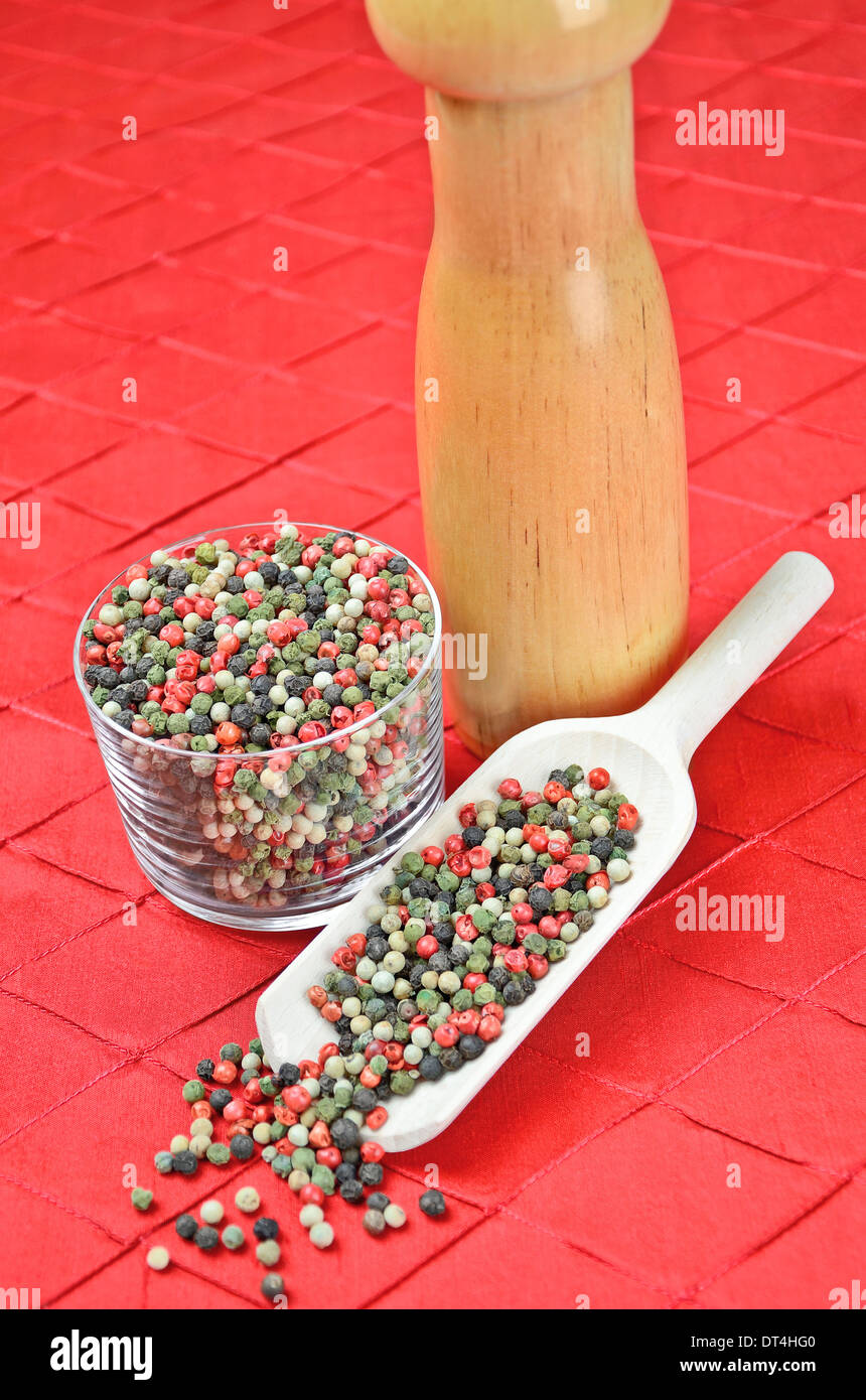 Mixed peppercorns in a glass and in a scoop on a red textile. Pink, black, green and white pepper Stock Photo