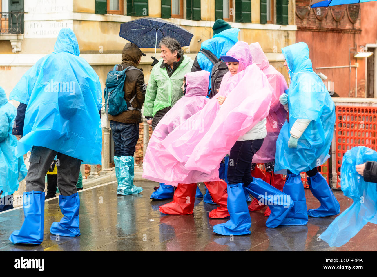 Venice, Italy. People in wet weather clothing, rain ponchos, and rain boots, standing on bridge during rain. Stock Photo