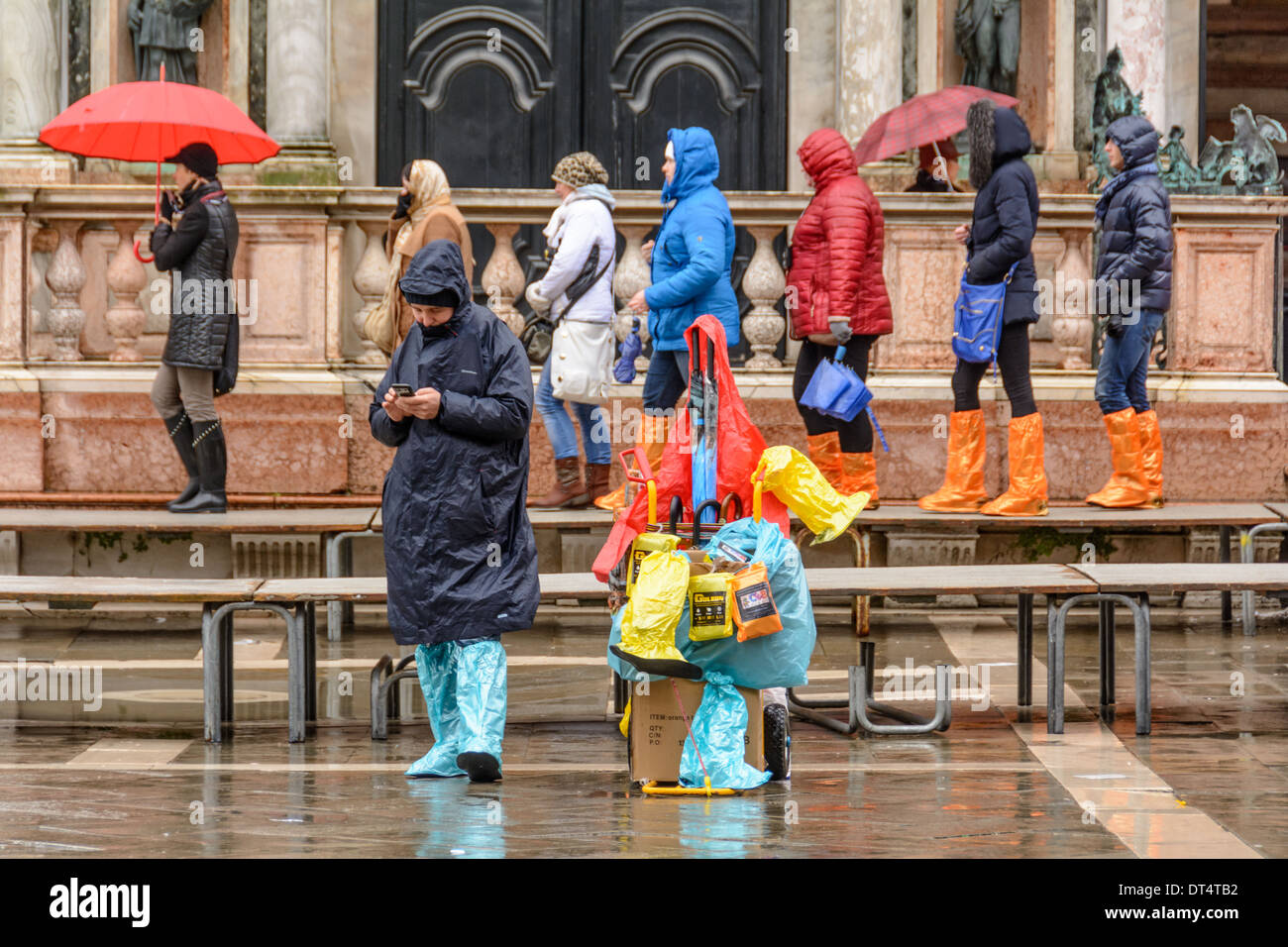 Venice, Italy. People walking on acqua alta gangway, vendor selling rainwear and rain boots on St Mark´s Square. Stock Photo