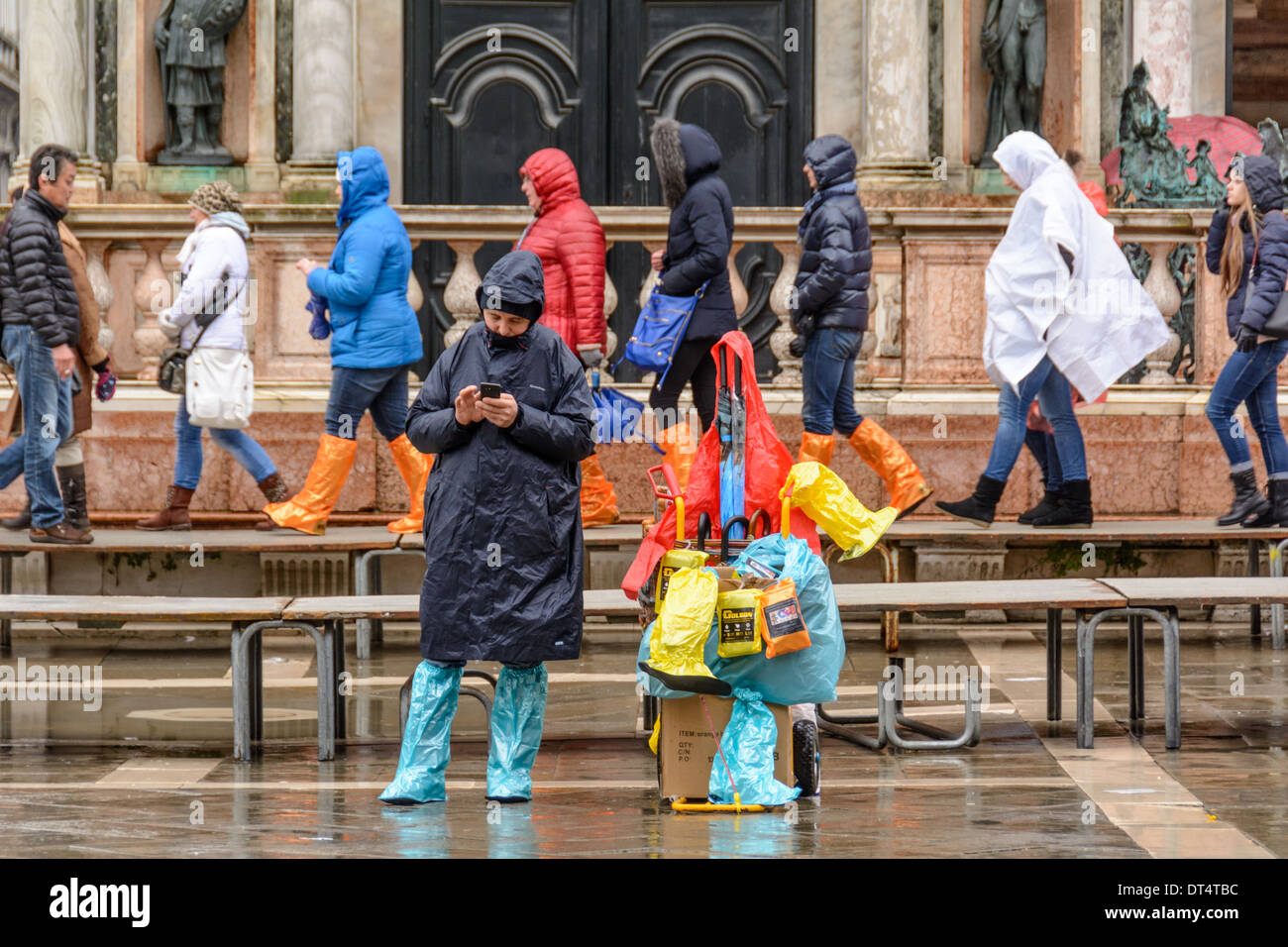 Venice, Italy. People walking on acqua alta gangway, vendor selling rainwear and rain boots on St Mark´s Square. Stock Photo