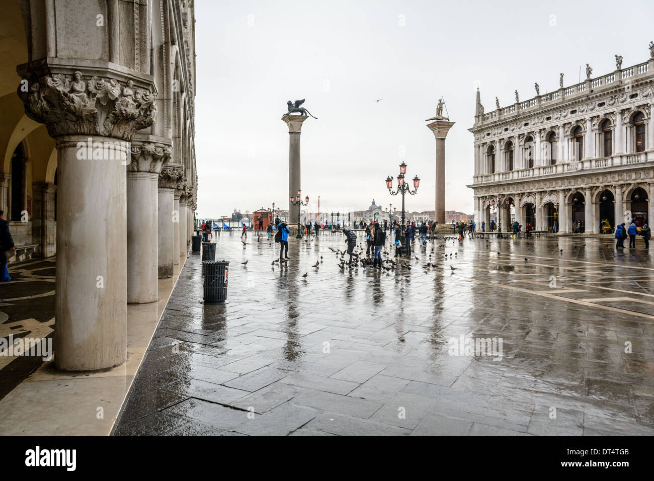 Venice, Italy. View over the Piazzetta di San Marco with two columns and tourists in rainwear feeding pigeons on a rainy day. Stock Photo