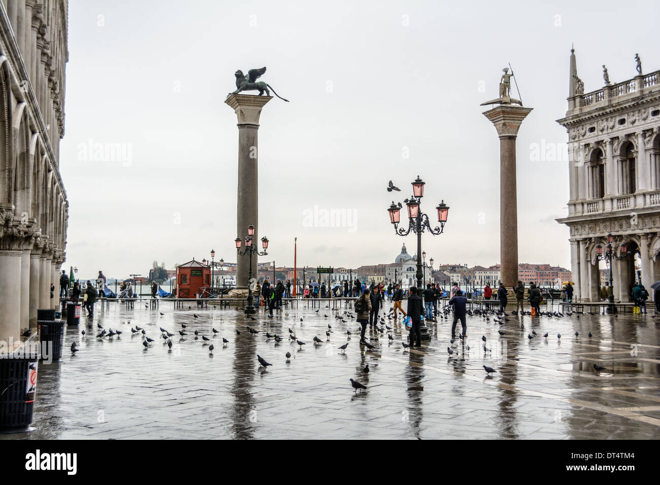 Venice, Italy. View over the Piazzetta di San Marco with two columns and tourists in rainwear feeding pigeons on a rainy day. Stock Photo
