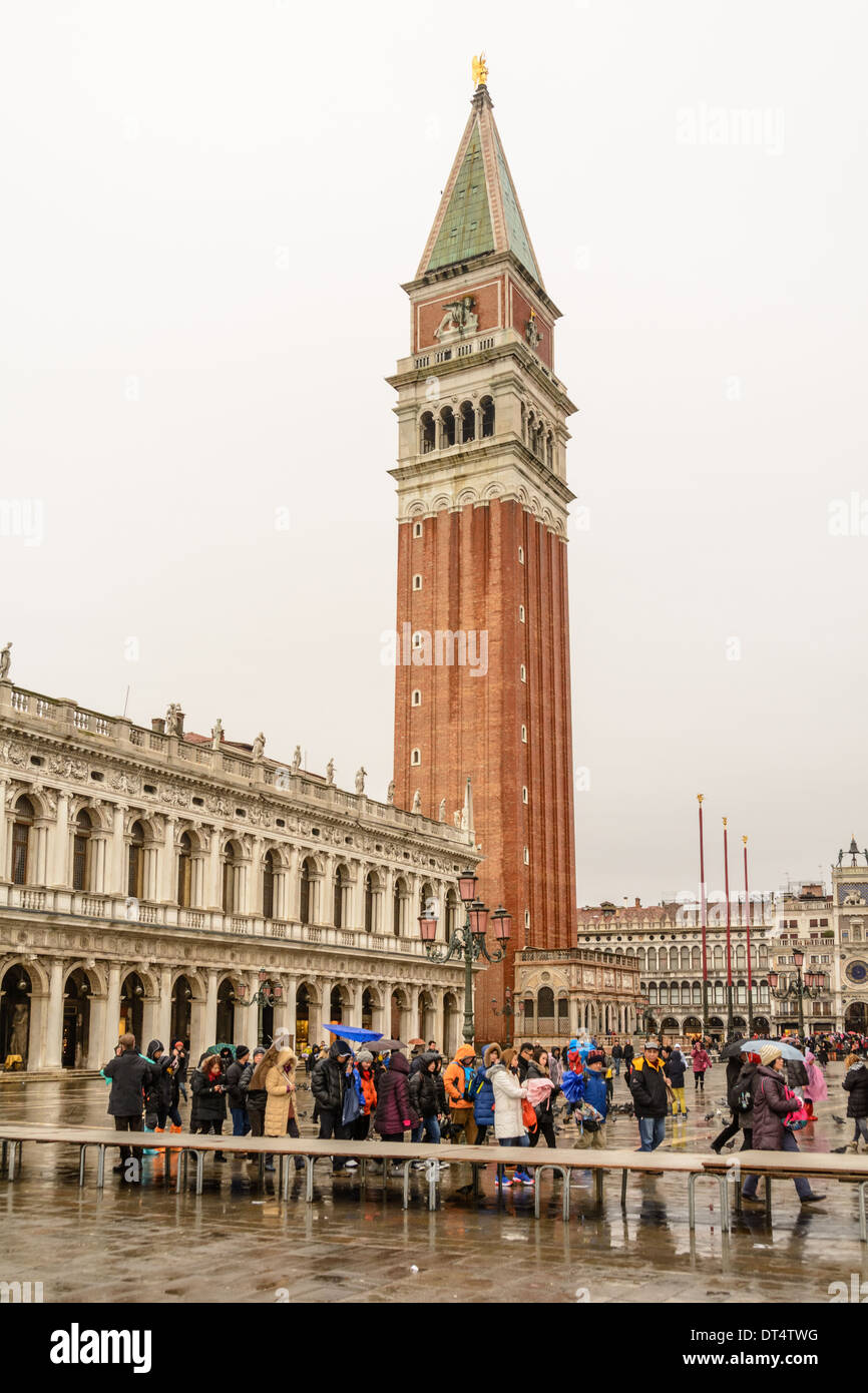 Venice, Italy. Campanile di San Marco belltower on the Piazzetta di San Marco at a rainy day with acqua alta gangways and tourists with umbrellas and wet weather clothing. Stock Photo