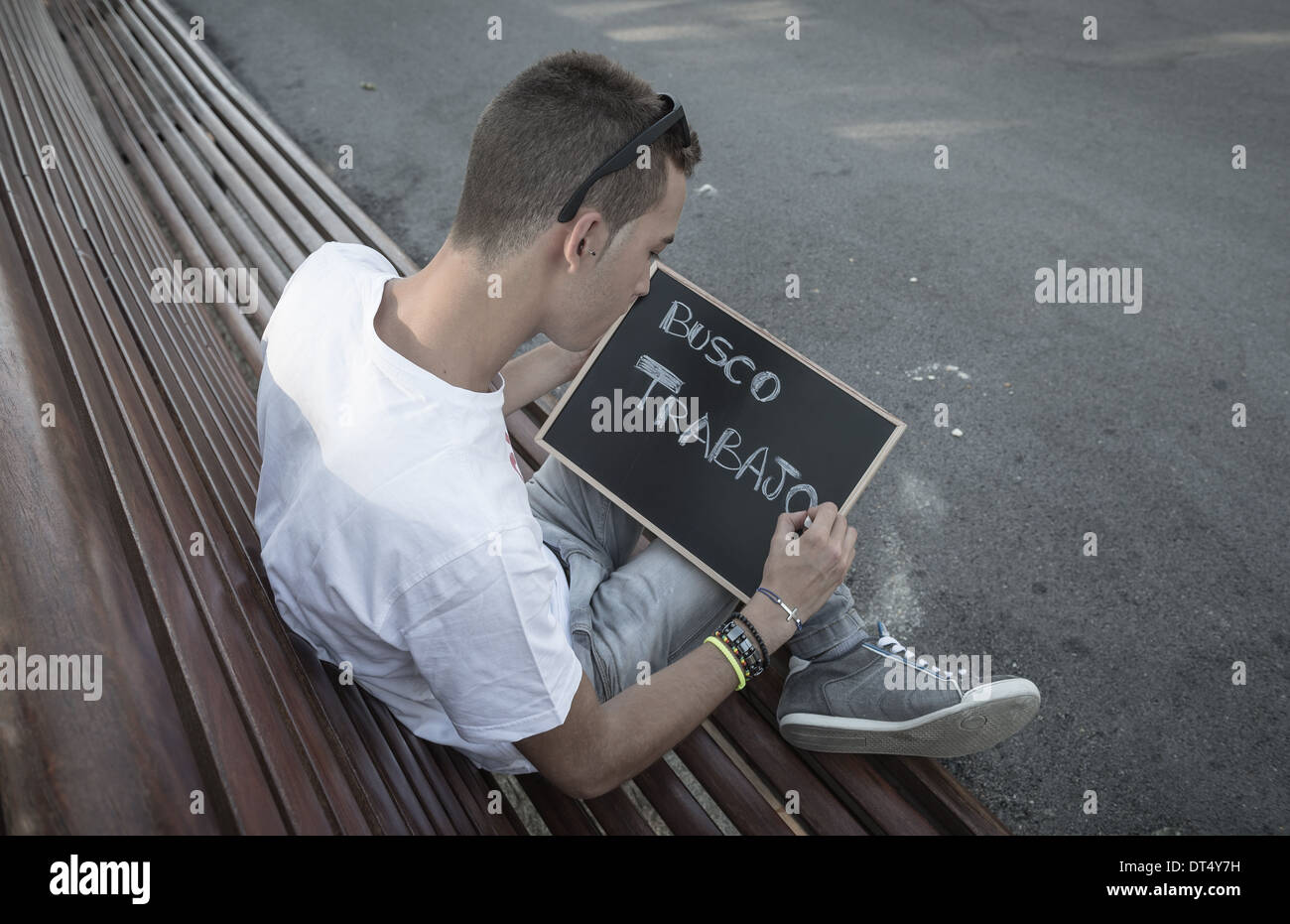 Young man writing I need job in spanish on a blackboard Stock Photo
