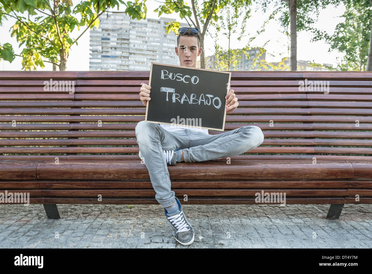 Young man writing I need job in spanish on a blackboard Stock Photo