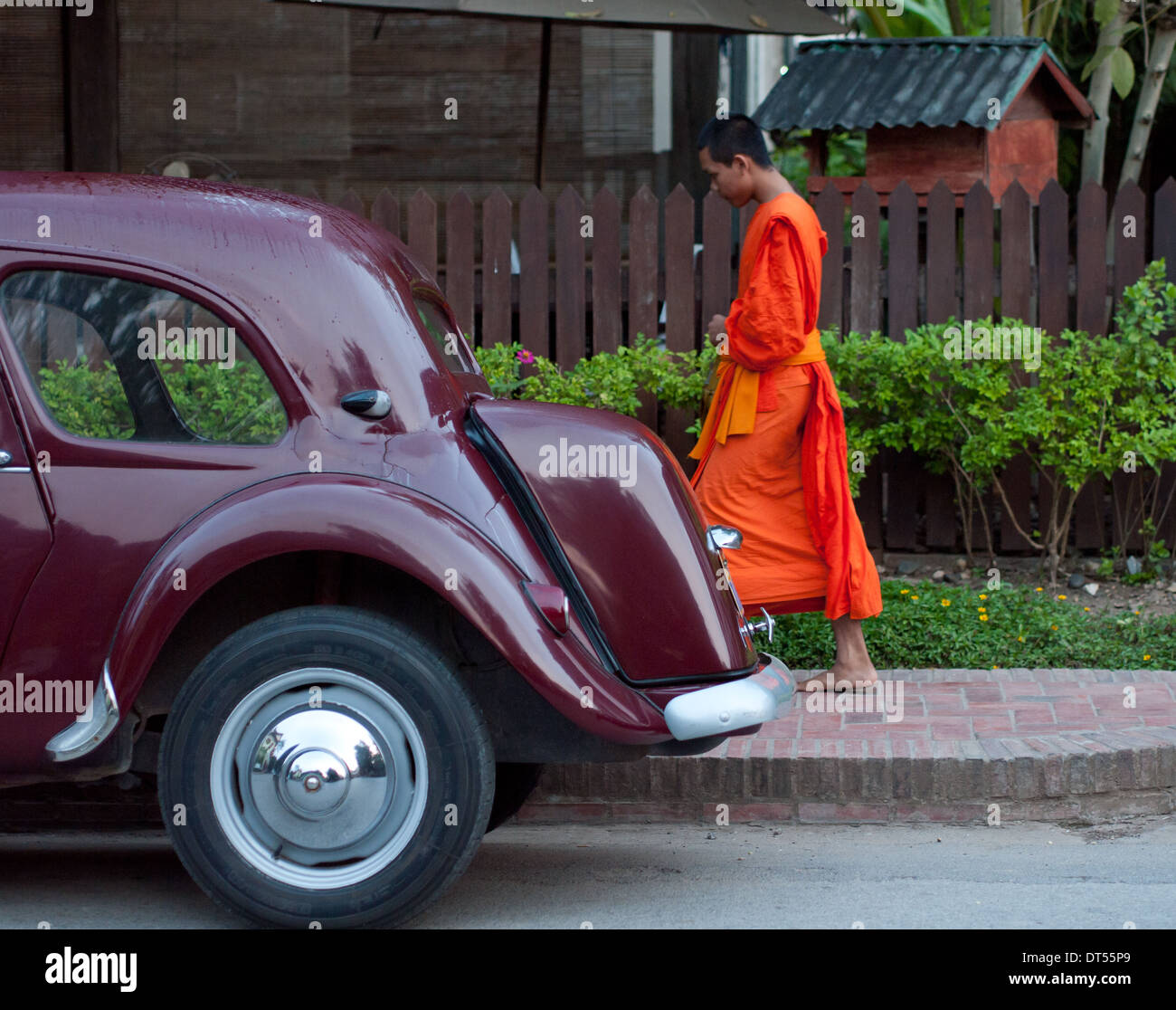 A Buddhist monk walks past an antique car during morning procession of alms in Luang Prabang, Laos. Stock Photo