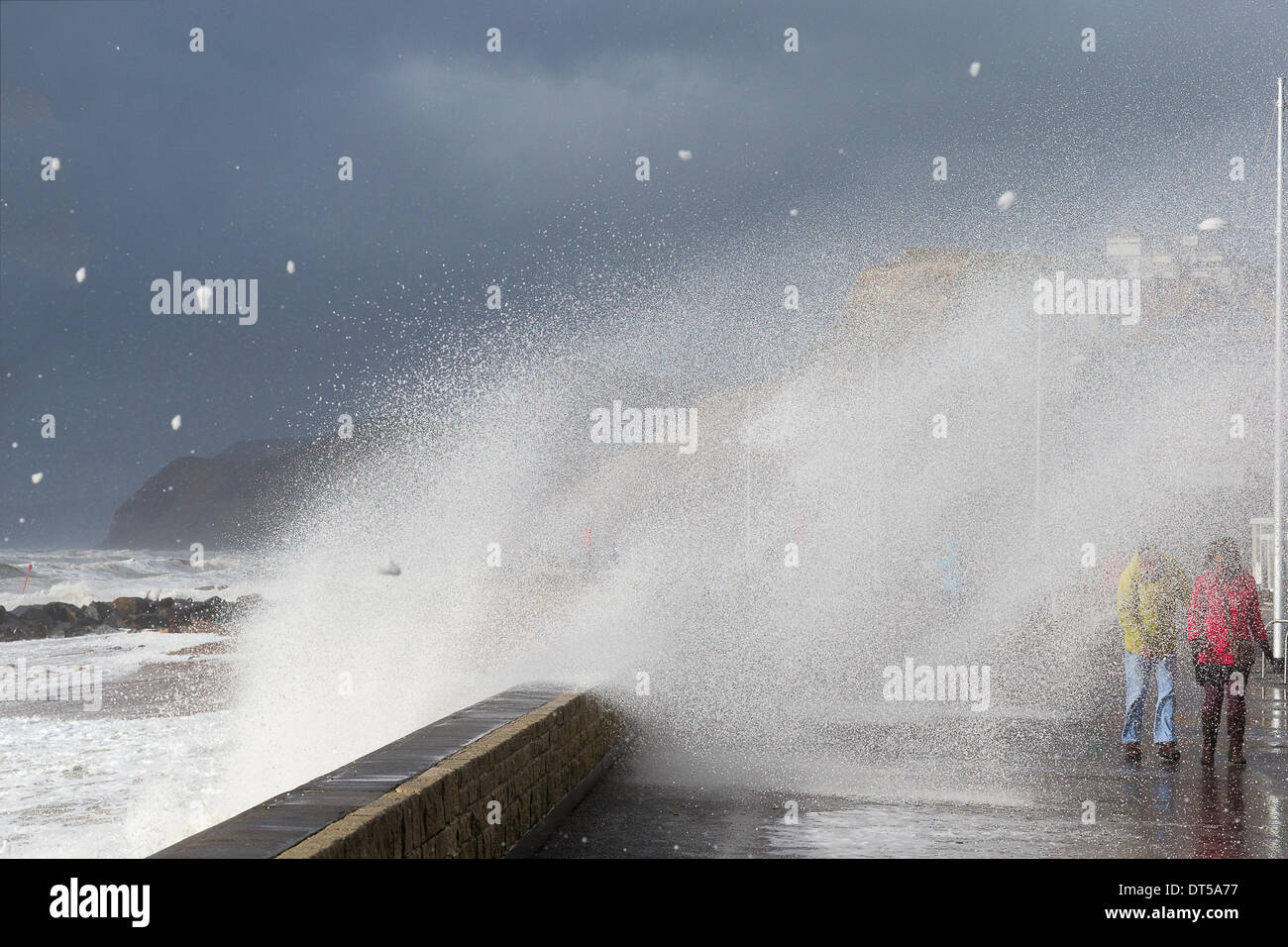 West Bay, Bridport, Dorset, United Kingdom at 13:12 hrs on 8th Feb 2014. During ferocious storms waves broke over the sea wall at high tide, throwing debris onto the sea front and drenching adventurous onlookers.  The extreme conditions were brought about by one of a continuing string of low pressure systems bringing associated high winds and weather fronts. Credit:  Living Levels Photography/Alamy Live News Stock Photo