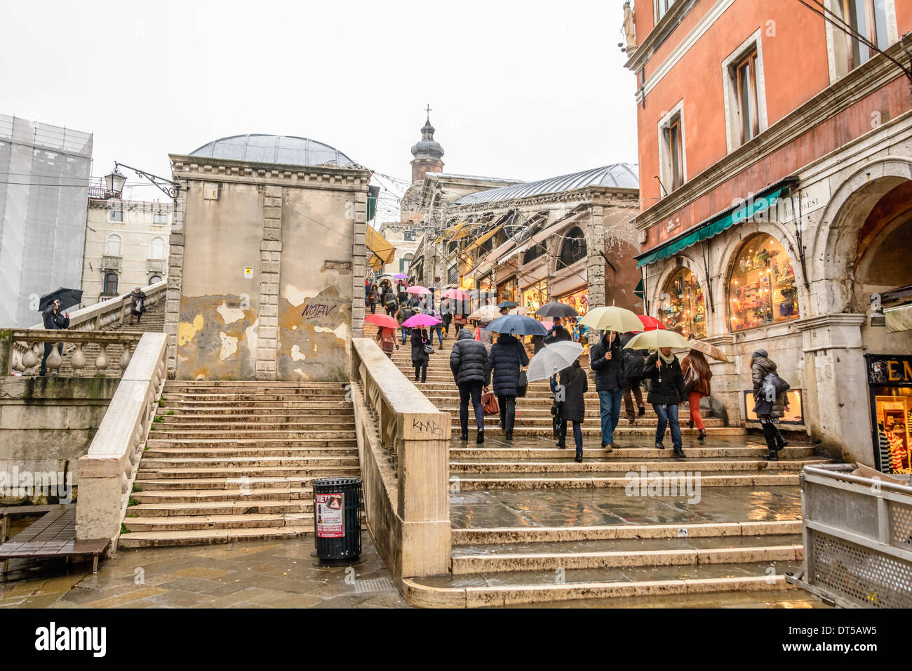Venice, Italy. People with umbrellas and wet weather clothing crossing the Rialto Bridge at a rainy day, overcast sky. Stock Photo