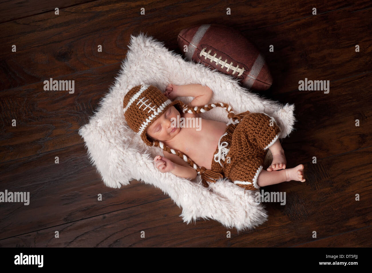 A 12 day old newborn baby boy sleeping in a fur lined crate and wearing a crocheted American football costume. Stock Photo
