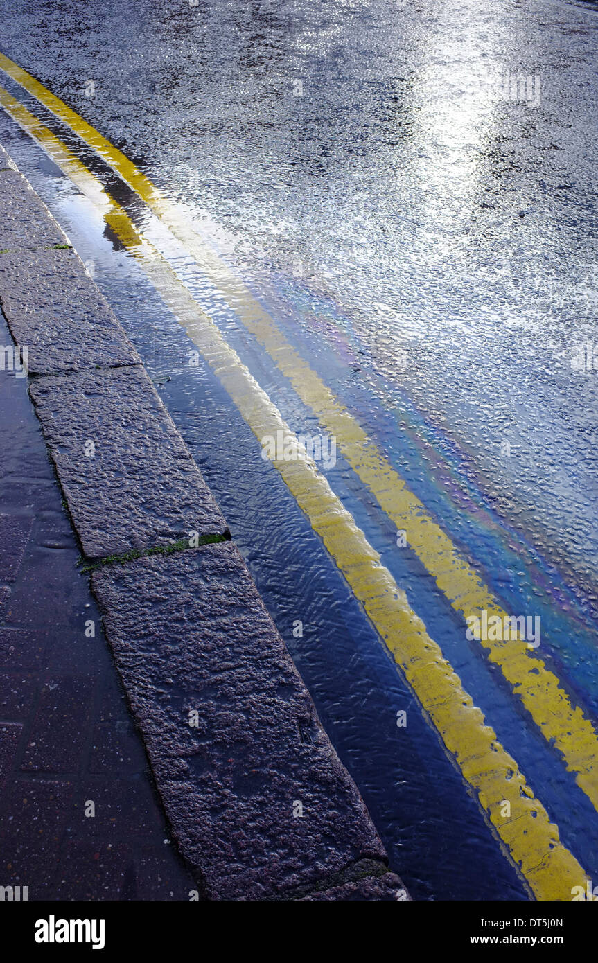 double yellow line on wet road with oil slick forming rainbow pattern Stock Photo