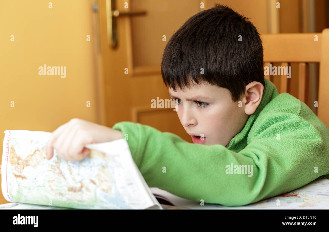 bored and tired boy doing homework from school in workbook using worl map Stock Photo