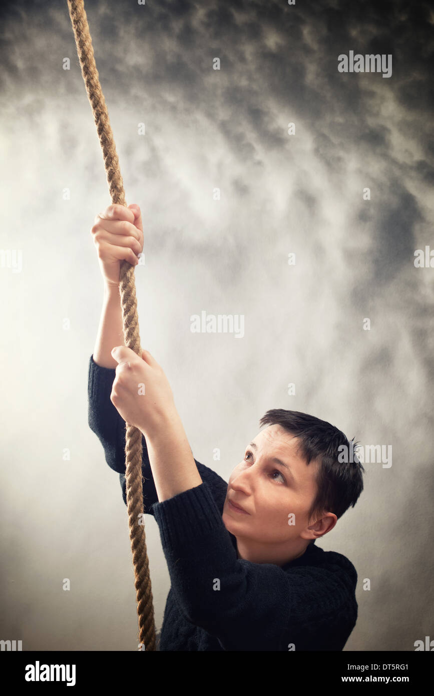 Woman climbing up with rope. Overcoming problems, obstacles and difficulties in life metaphor. Stock Photo
