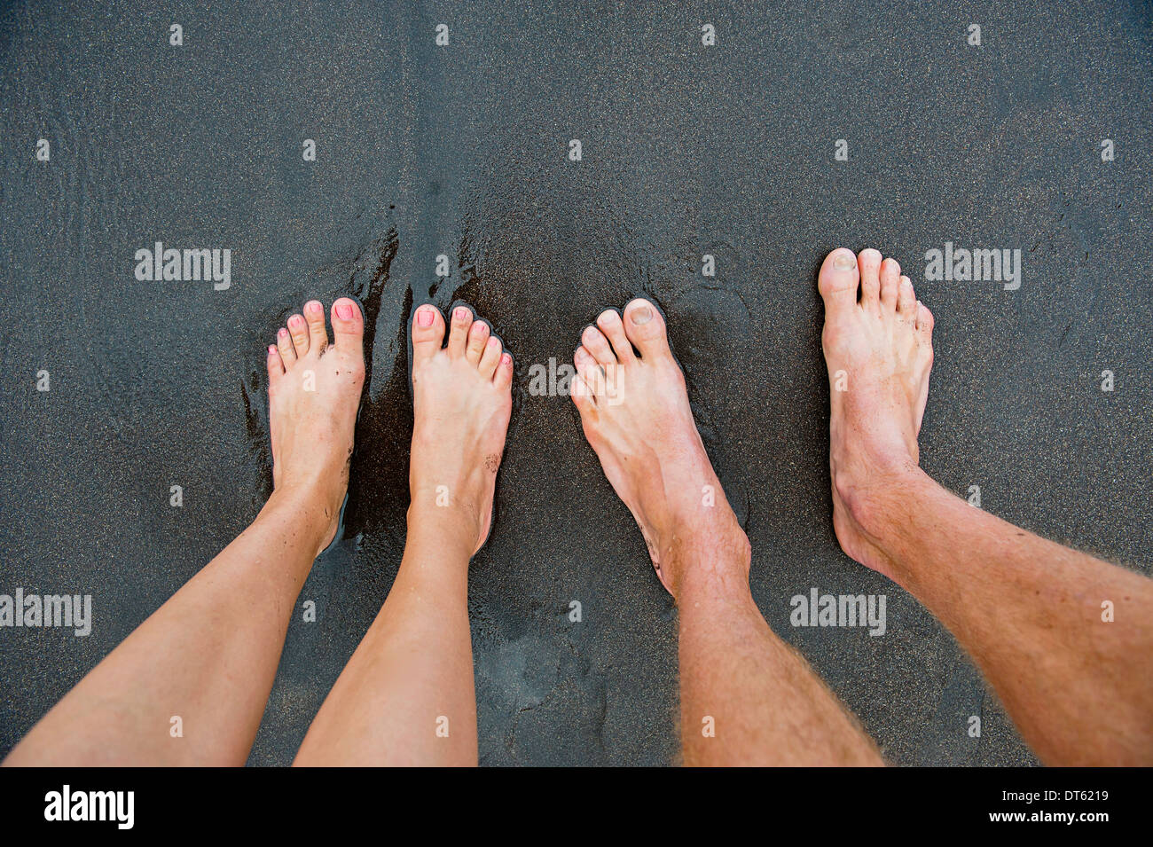 Pairs of male and female feet on black sand Stock Photo