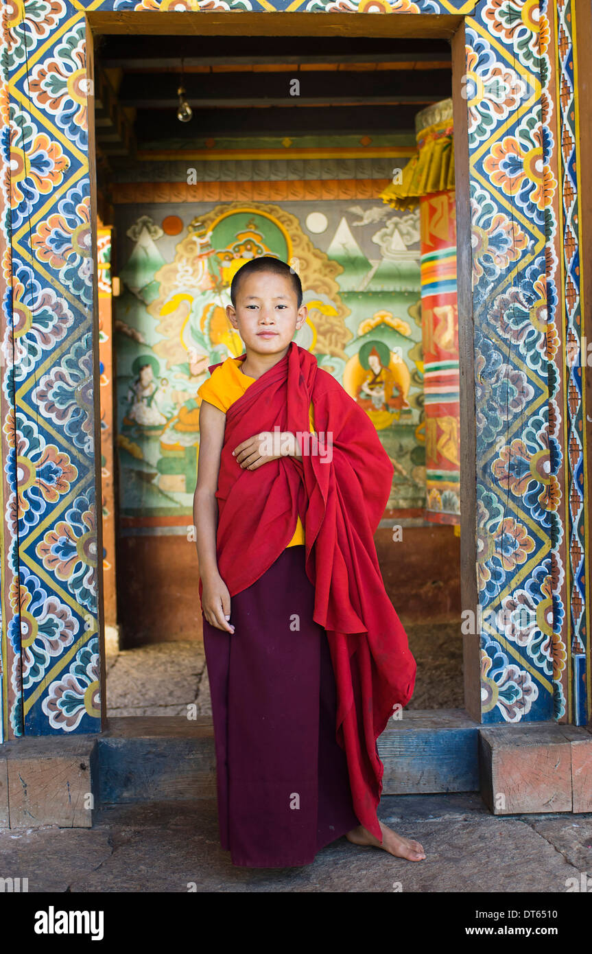 Bhutan, South Asia, Punakha, Single young novice boy monk standing in doorway of Chimi Lakhang temple in the old capital. Stock Photo