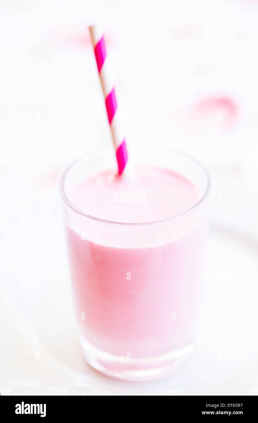 Closeup of raspberry smoothie made with milk and ice cream and with striped white and pink straw in glass on light background Stock Photo