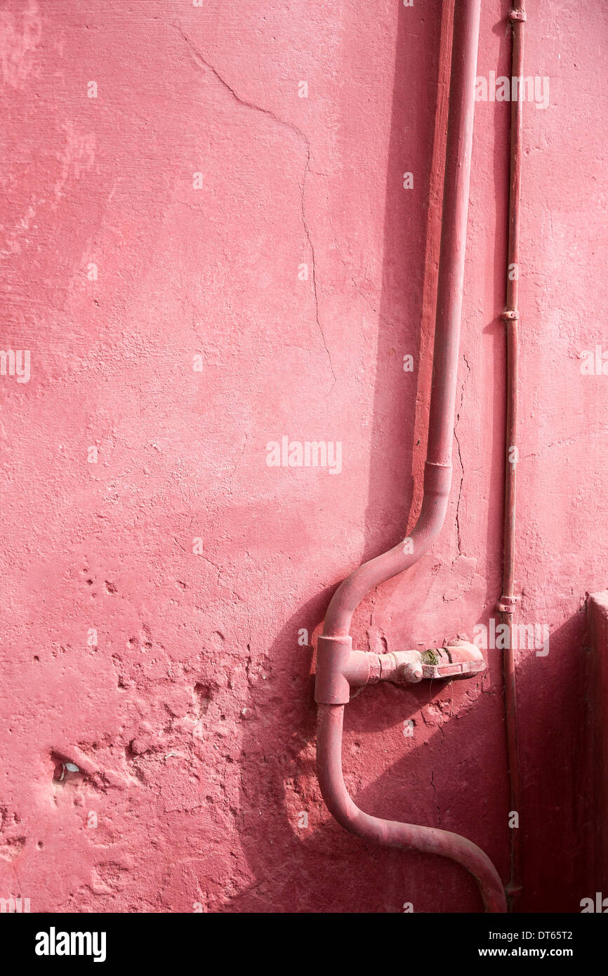Pink wall with a water pipe and electric cable running down it, also painted pink Stock Photo